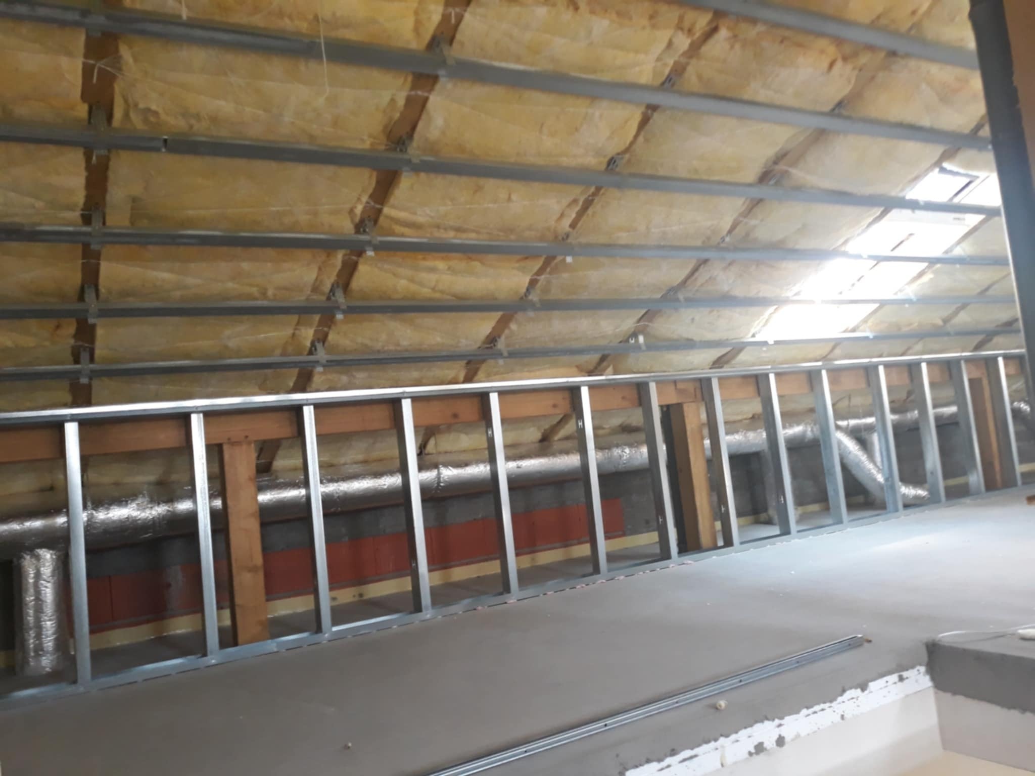 Konstrukcja metalowa ścianki działowej na poddaszu, widoczna izolacja stropu wełną mineralną i fragment instalacji wentylacyjnej.