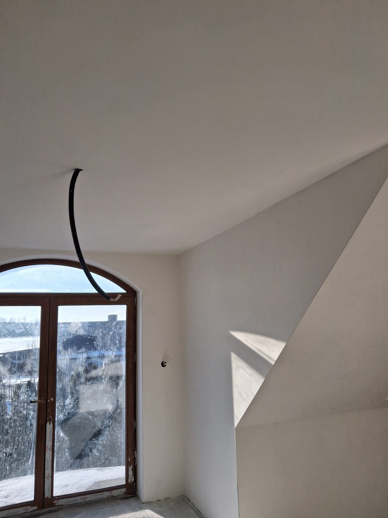 Poddasze po szpachlowaniu, widoczne gładkie ściany i sufit, okno z drewnianą ramą. W suficie wystaje rura instalacyjna. Świeże, jasne wnętrze.