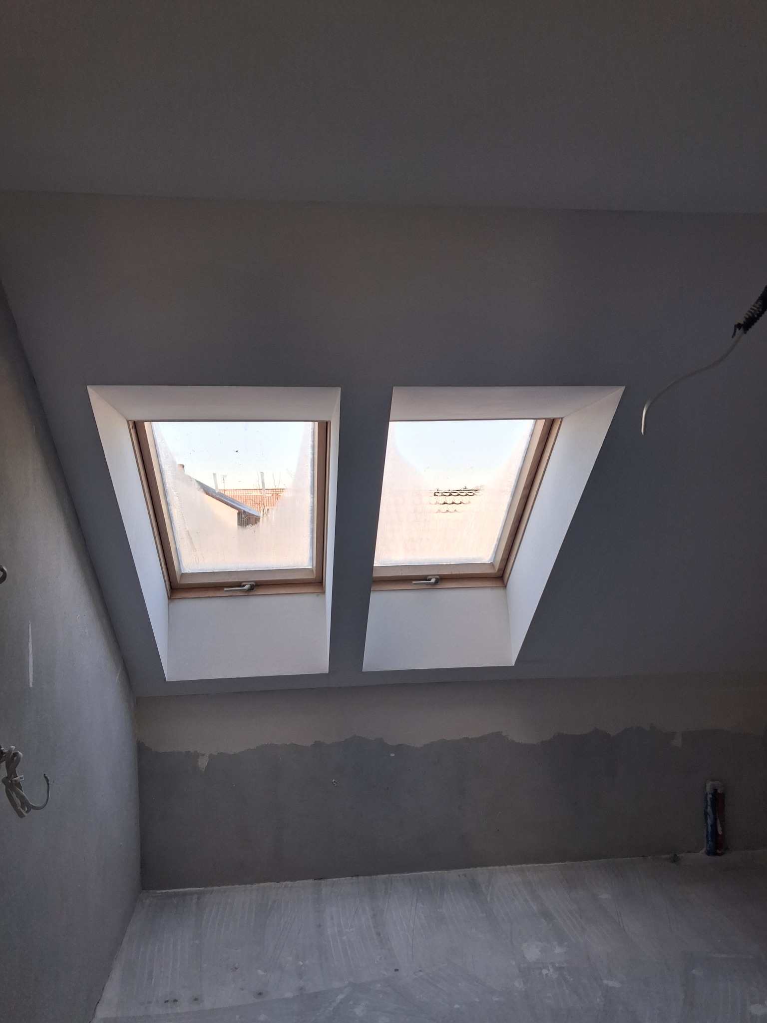 Poddasze z dwoma oknami dachowymi po szpachlowaniu, ściany przygotowane do dalszych prac wykończeniowych. Widoczne niedoskonałości powierzchni.