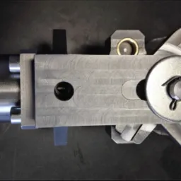 Precyzyjnie obrobiony, metalowy uchwyt tokarski z widocznymi śladami obróbki skrawaniem, sfotografowany z góry na ciemnym tle.