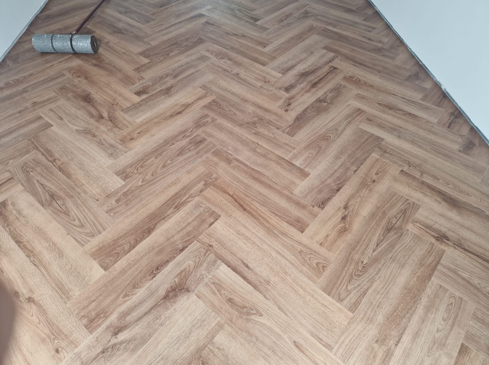 Ułożona podłoga z paneli w jasnym odcieniu drewna, wzór jodełka francuska, widoczny wałek malarski w rogu pomieszczenia.