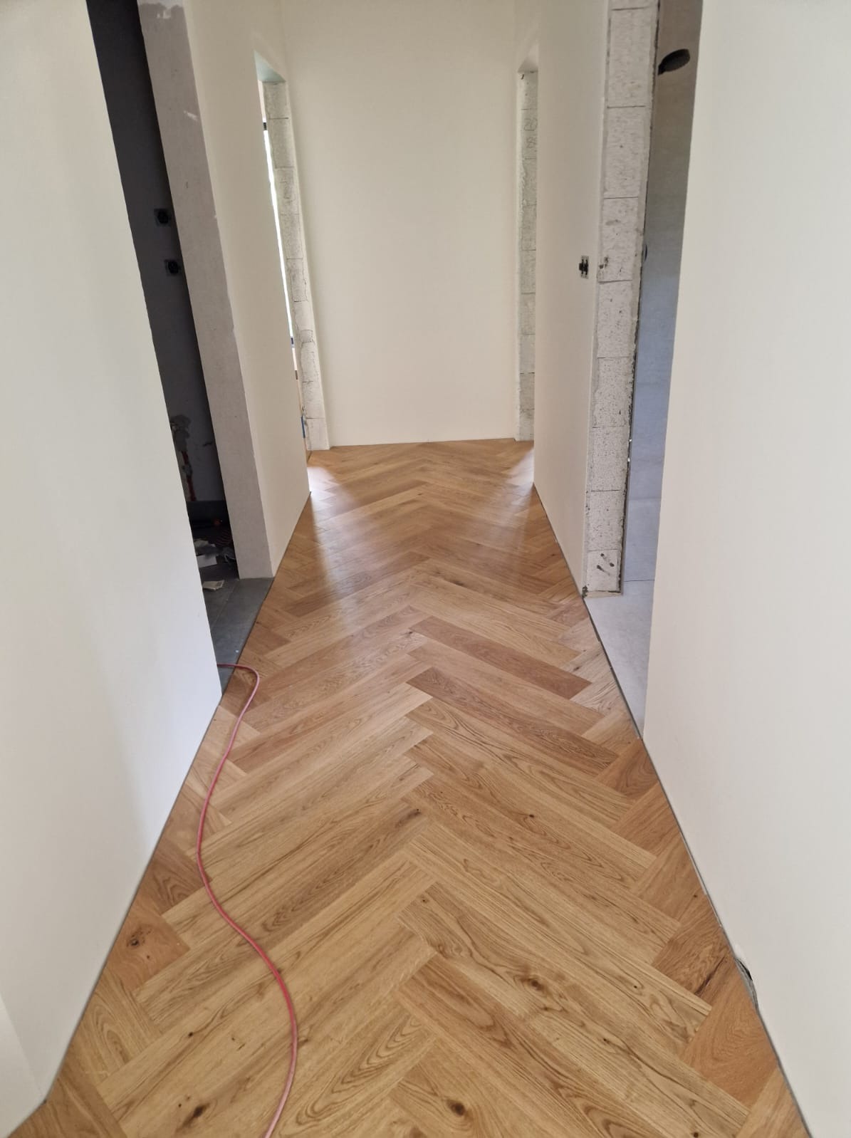 Ułożona parkiet w jodełkę w korytarzu w Białymstoku, widoczne surowe ściany i czerwony kabel na podłodze w trakcie wykańczania wnętrza.