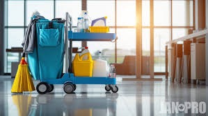 Wózek do sprzątania z pełnym wyposażeniem: środki czystości, szczotka, mop, wiadro, na tle lśniącej posadzki i okien z widokiem na lotnisko.