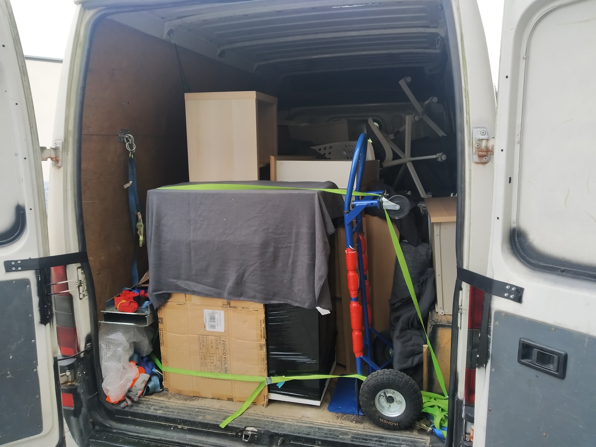 Wnętrze białego busa załadowane meblami i kartonami zabezpieczonymi zielonymi pasami transportowymi, widoczny wózek transportowy, realizacja z Krakuszowic.