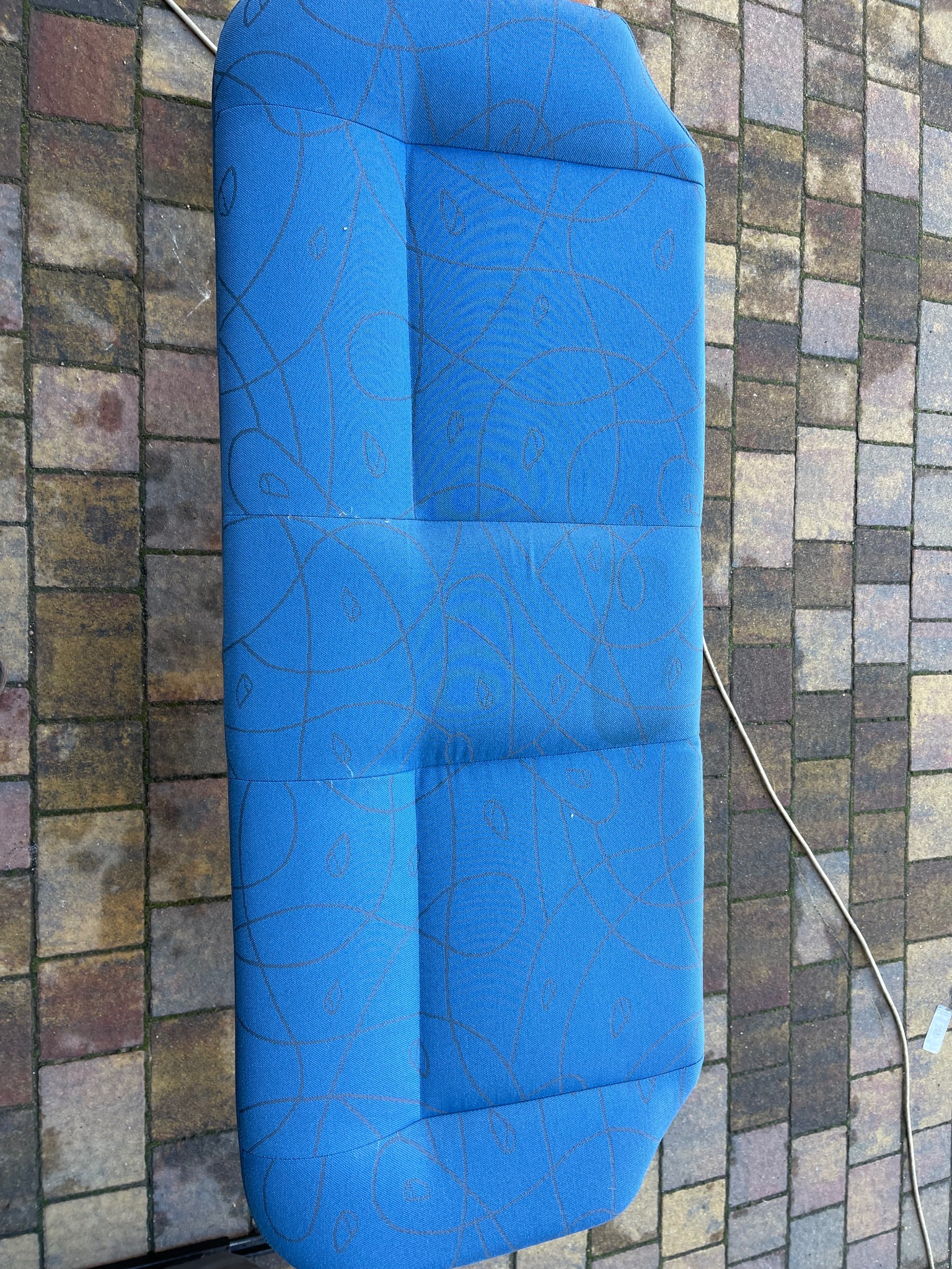 Niebieskie siedzisko samochodowe z wzorem na brukowanej powierzchni, widoczny kabel elektryczny.