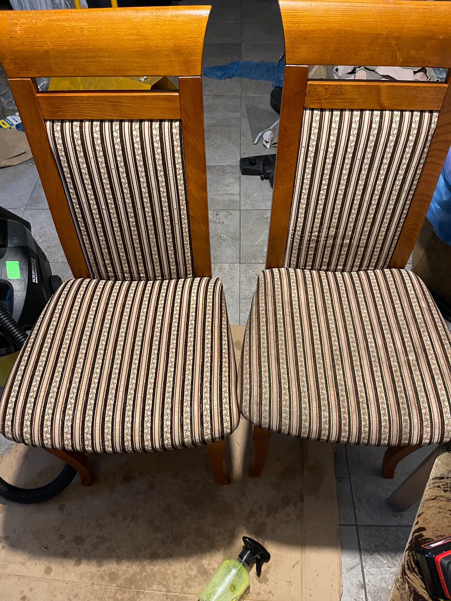 Dwa drewniane krzesła z tapicerowanymi siedziskami i oparciami w brązowo-białe paski, widoczne ślady czyszczenia i butelka ze środkiem czyszczącym w pobliżu.