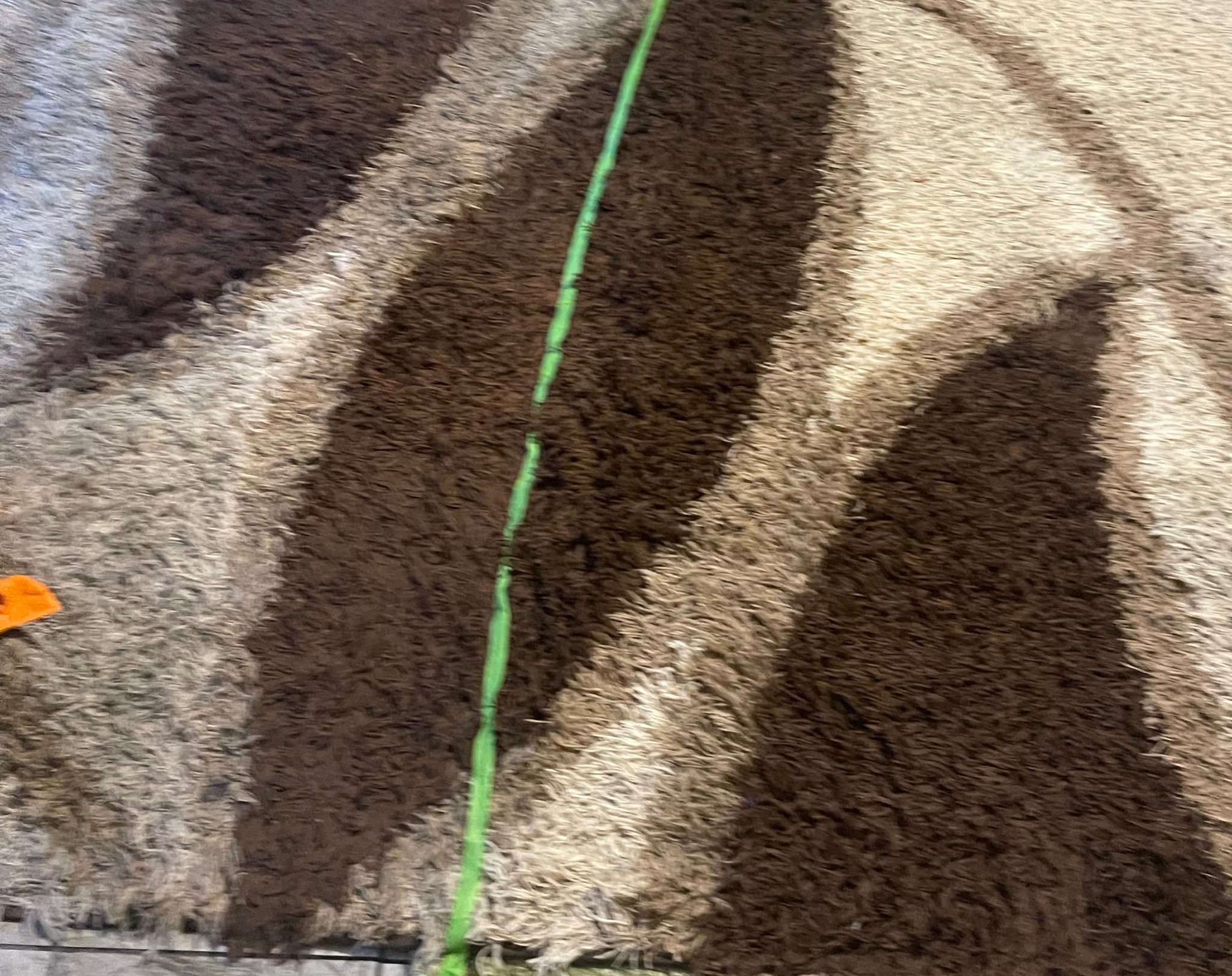 Wielobarwny, puszysty dywan z ciemnymi i jasnymi pasami, z widoczną zieloną liną na jego powierzchni.