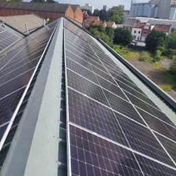 Sun Force - Instalacja paneli słonecznych na dachu budynku przemysłowego, widok z góry, w tle zabudowa miejska i drzewa.