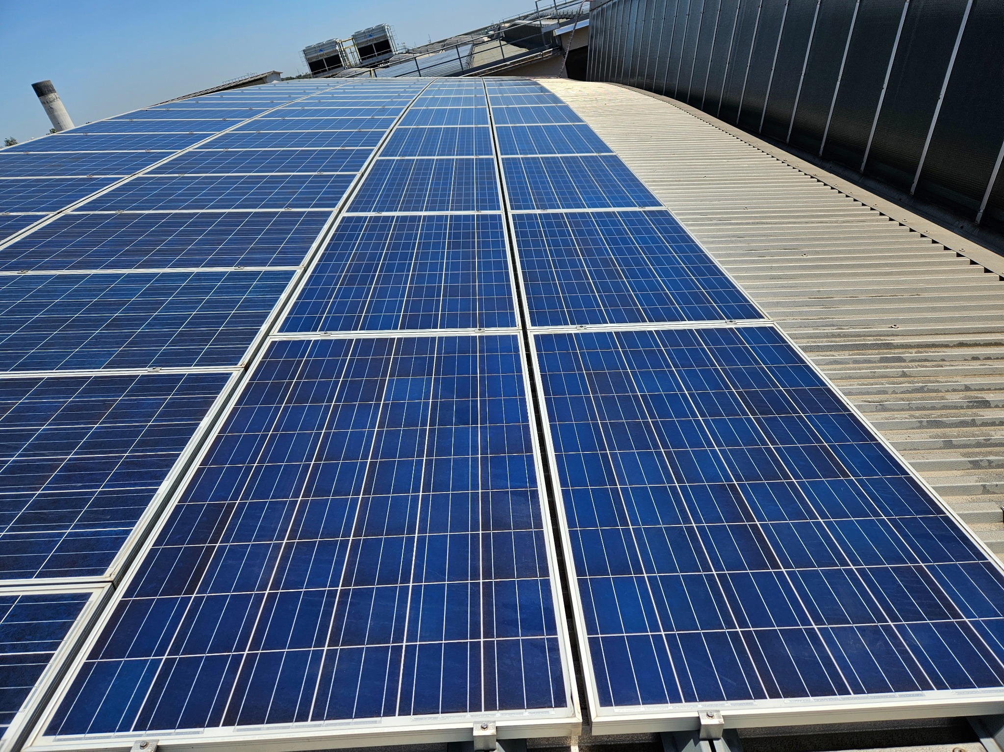 Instalacja fotowoltaiczna na dachu z blachy trapezowej, widoczne panele w układzie rzędowym oraz elementy wentylacyjne w tle.