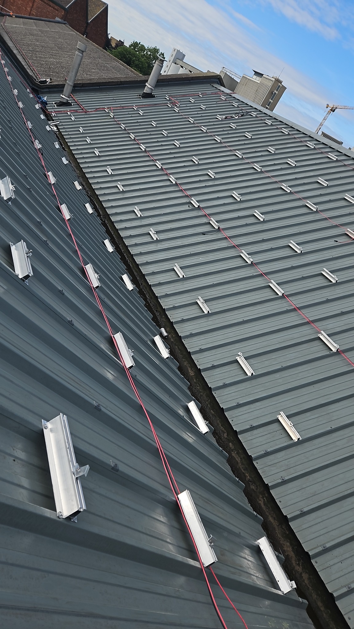 Metalowy dach z zamontowanymi elementami mocującymi pod panele słoneczne i przewodami, widok z góry pod kątem.