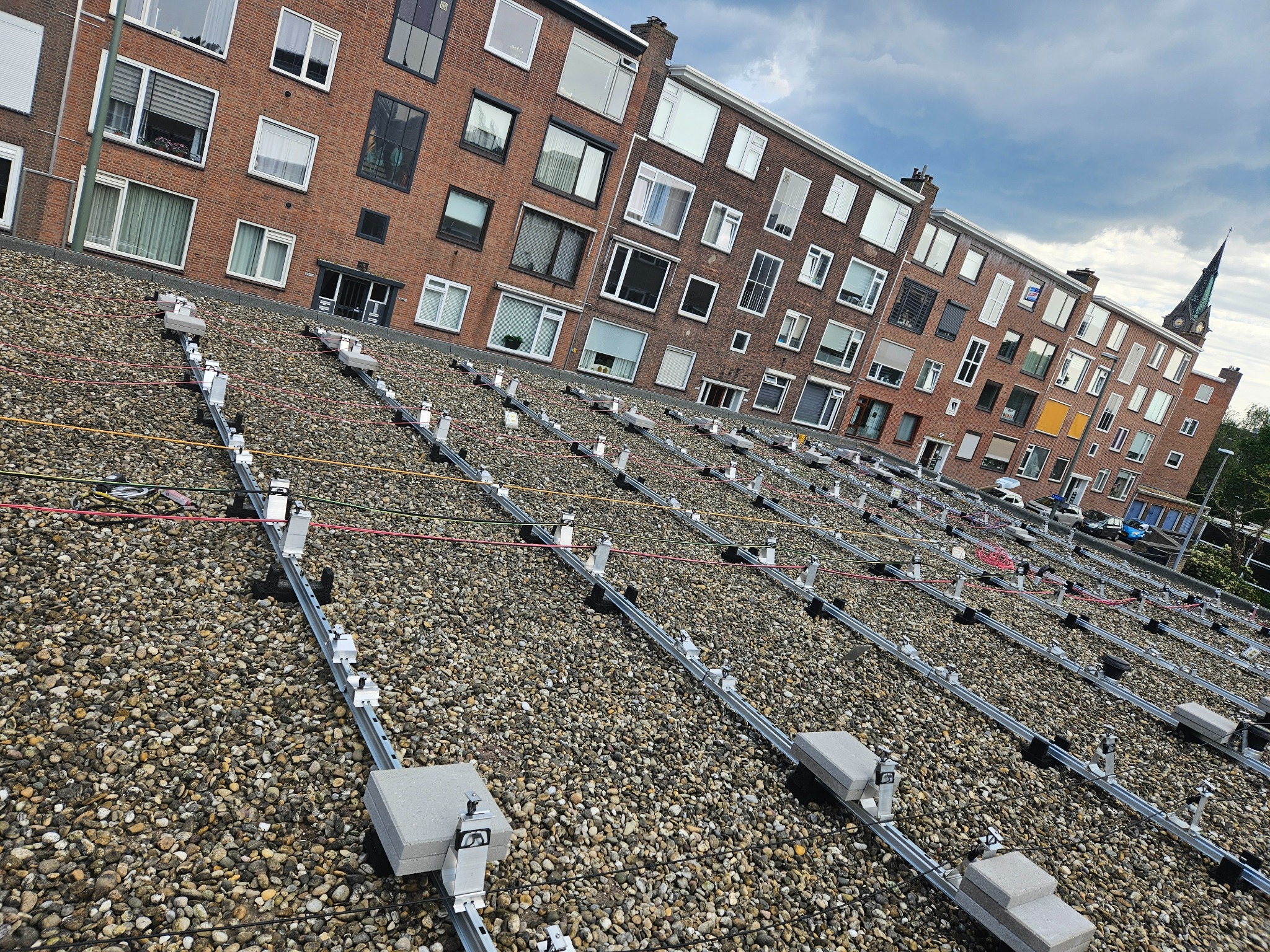 Montaż konstrukcji wsporczej pod panele słoneczne na płaskim, żwirowym dachu budynku mieszkalnego w Bałtowie, widok z góry na szyny i uchwyty przed instalacją paneli.