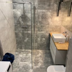 Mateusz Zakrzewski - Nowoczesna łazienka we Wrocławiu z szarymi płytkami imitującymi beton, kabiną prysznicową typu walk-in, umywalką nablatową na drewnianym blacie i wiszącą toaletą.