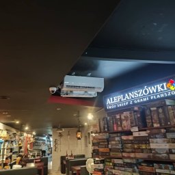 Anemos Bartosz Naskręt - Wnętrze sklepu z grami planszowymi: widoczna klimatyzacja kasetonowa zamontowana pod sufitem, regały wypełnione grami, oświetlenie punktowe i dekoracyjne lampy wiszące.