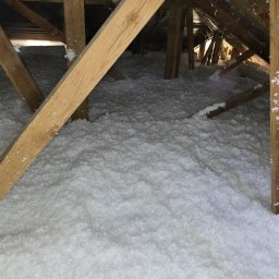 ADMAR Mariusz Pedda - Poddasze ocieplone białą wełną mineralną, widoczne drewniane krokwie i fragment dachu z blachy trapezowej.