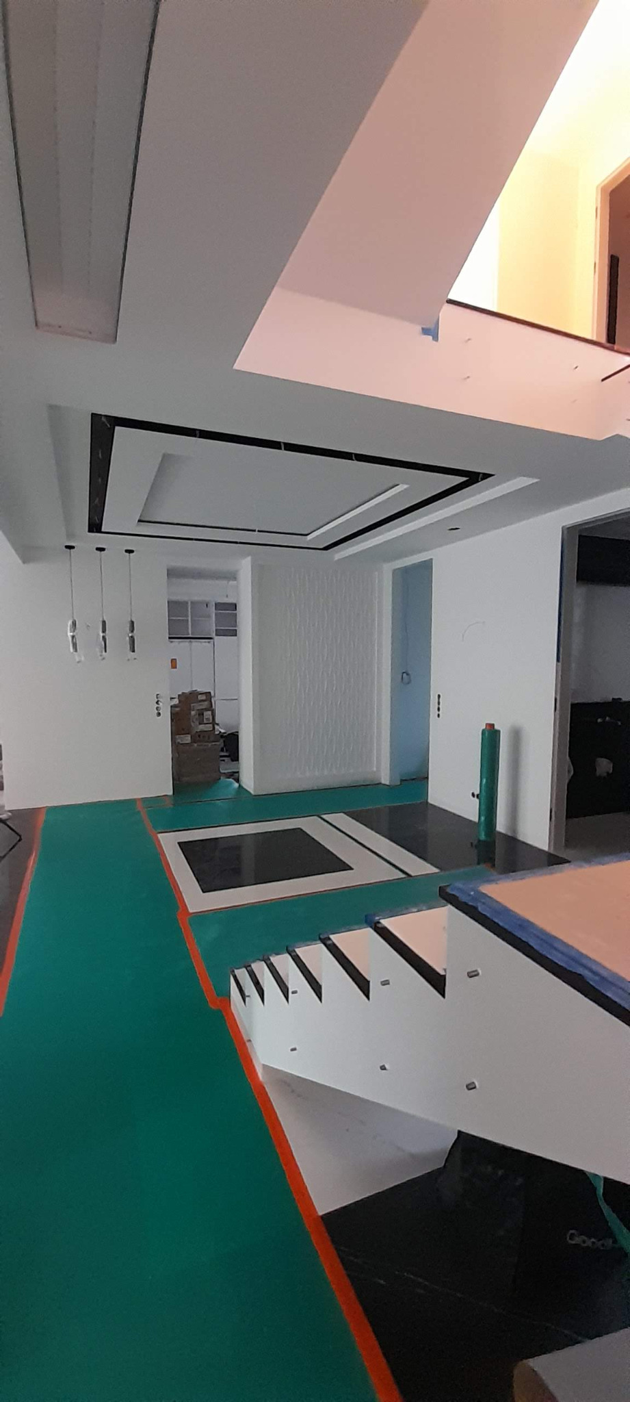 Wnętrze w trakcie prac wykończeniowych: zabezpieczona podłoga, widoczne schody, sufit podwieszany z oświetleniem.