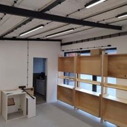 6EL - Wnętrze w trakcie remontu z widocznymi instalacjami elektrycznymi poprowadzonymi po suficie w metalowych rurkach, częściowo zamontowane drewniane regały, białe ściany i szara podłoga, widoczna...