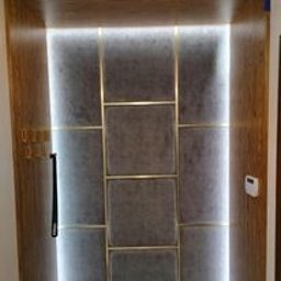 6EL - Panel wejściowy z szarego materiału, obramowany drewnem i podświetlony ledowym oświetleniem po bokach, z czarną klamką po lewej stronie i panelem sterowania po prawej.