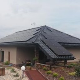 6EL - Dom jednorodzinny z panelami fotowoltaicznymi zamontowanymi na dachu z dachówki ceramicznej, widok z poziomu gruntu, pochmurne niebo.