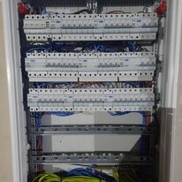 Rozdzielnica elektryczna z licznymi bezpiecznikami i przewodami wewnątrz obudowy, widoczne kable w różnych kolorach, ułożone warstwowo.