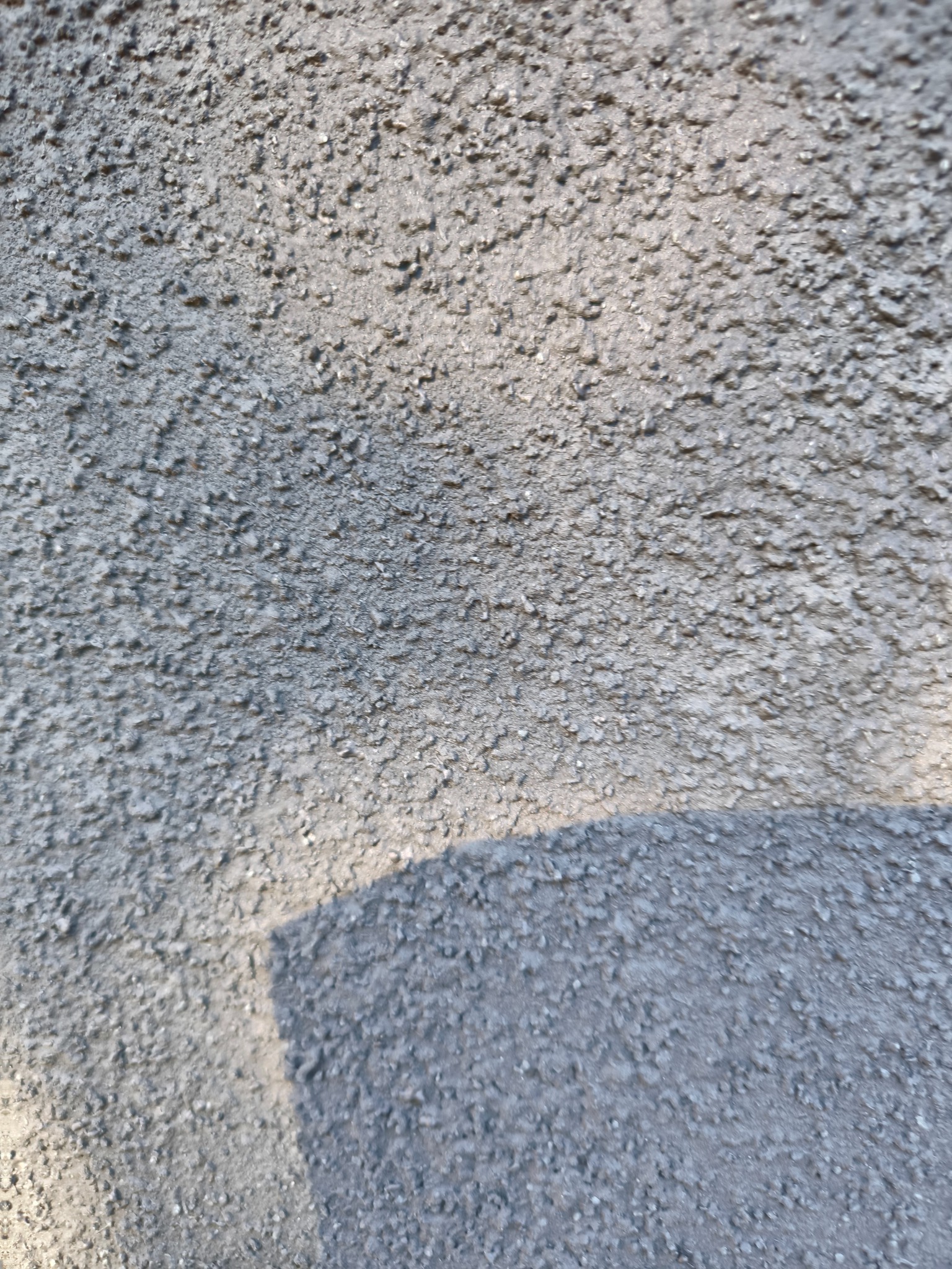 Szara, chropowata faktura elewacji w zbliżeniu, oświetlona naturalnym światłem z widocznym cieniem.