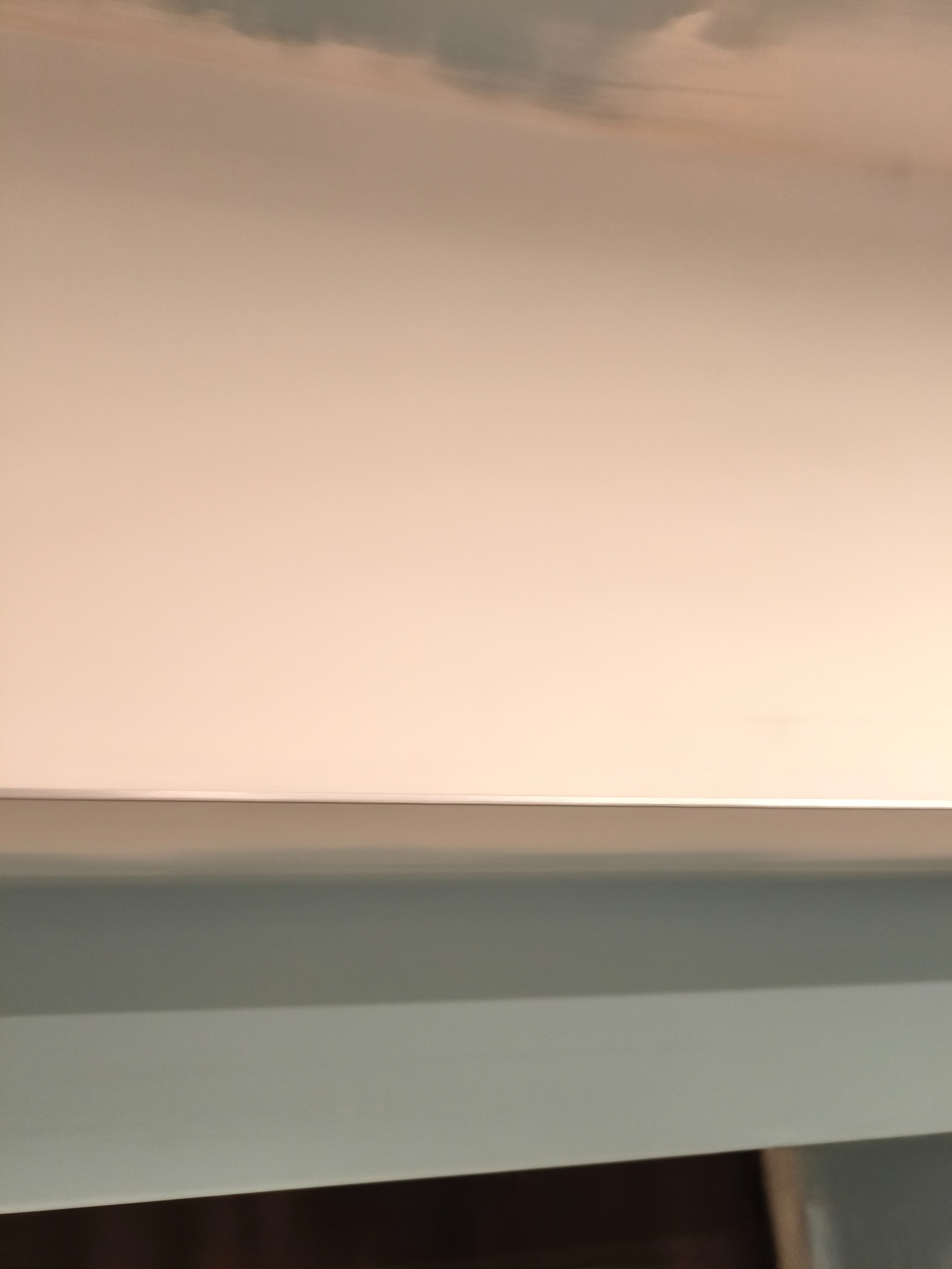 Świeżo pomalowany sufit na jasny, neutralny kolor, widoczne delikatne smugi farby i gładkie przejście do ściany w odcieniach szarości.