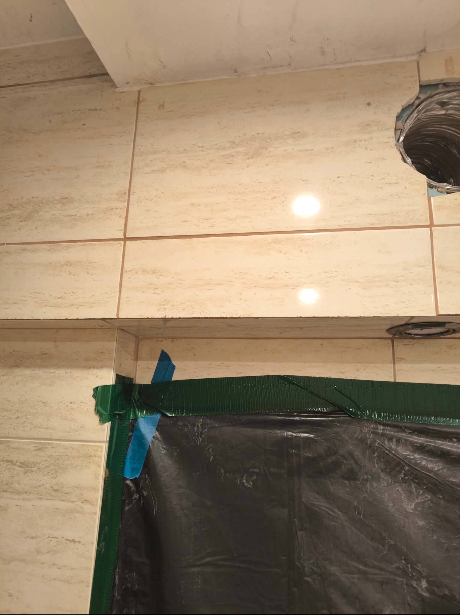 Przygotowanie do prac wykończeniowych w łazience: zabezpieczenie powierzchni folią i taśmą malarską przed zabrudzeniem, widoczny otwór wentylacyjny w ścianie z zamontowaną rurą.