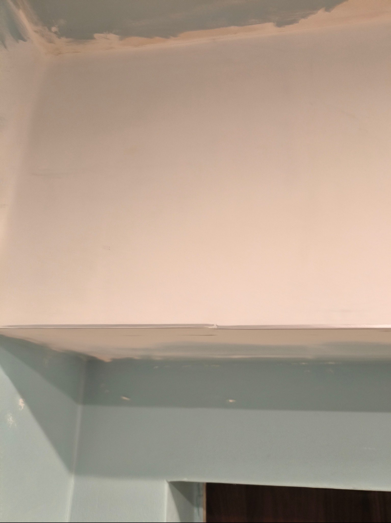 Fragment wnętrza w trakcie prac wykończeniowych; widoczna ściana i sufit po szpachlowaniu, ale przed ostatecznym malowaniem, z widocznymi niedoskonałościami i śladami po taśmie malarskiej.