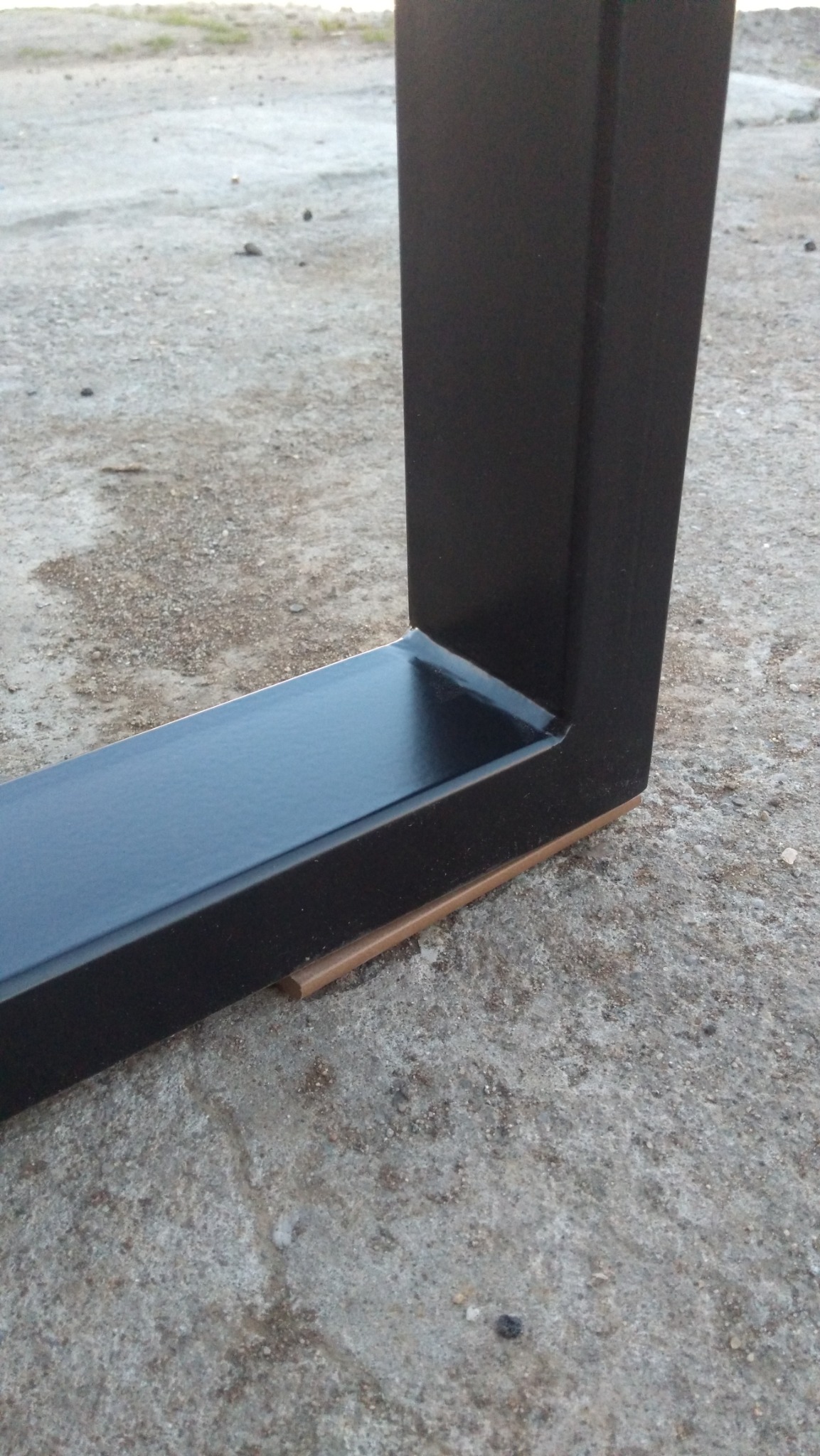 Fragment metalowej konstrukcji pomalowanej na czarno, prawdopodobnie elementu ogrodzenia lub balustrady, z widocznym spawem i podkładką dystansową.