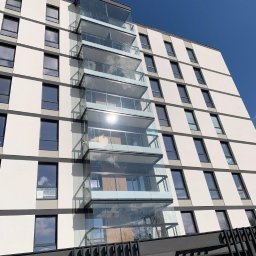 Cover Glass - Nowoczesny budynek z przeszklonymi balkonami i balustradami, widok z dołu w słoneczny dzień.