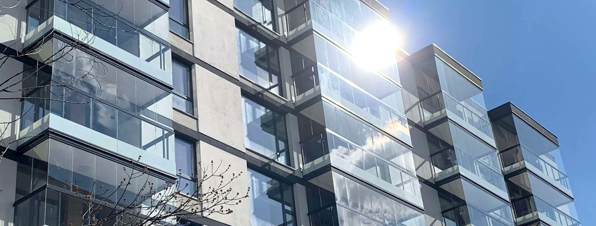 Nowoczesna zabudowa balkonu w bloku mieszkalnym z wykorzystaniem szkła refleksyjnego, odbijającego błękitne niebo i chmury.