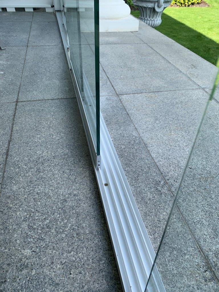 Szklana balustrada z białym profilem zamontowana na szarym tarasie, widok z bliska na mocowanie