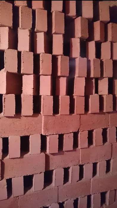 Ułożone cegły ceramiczne w magazynie, widoczne nieregularności w ułożeniu i odcieniach, oświetlenie magazynowe.