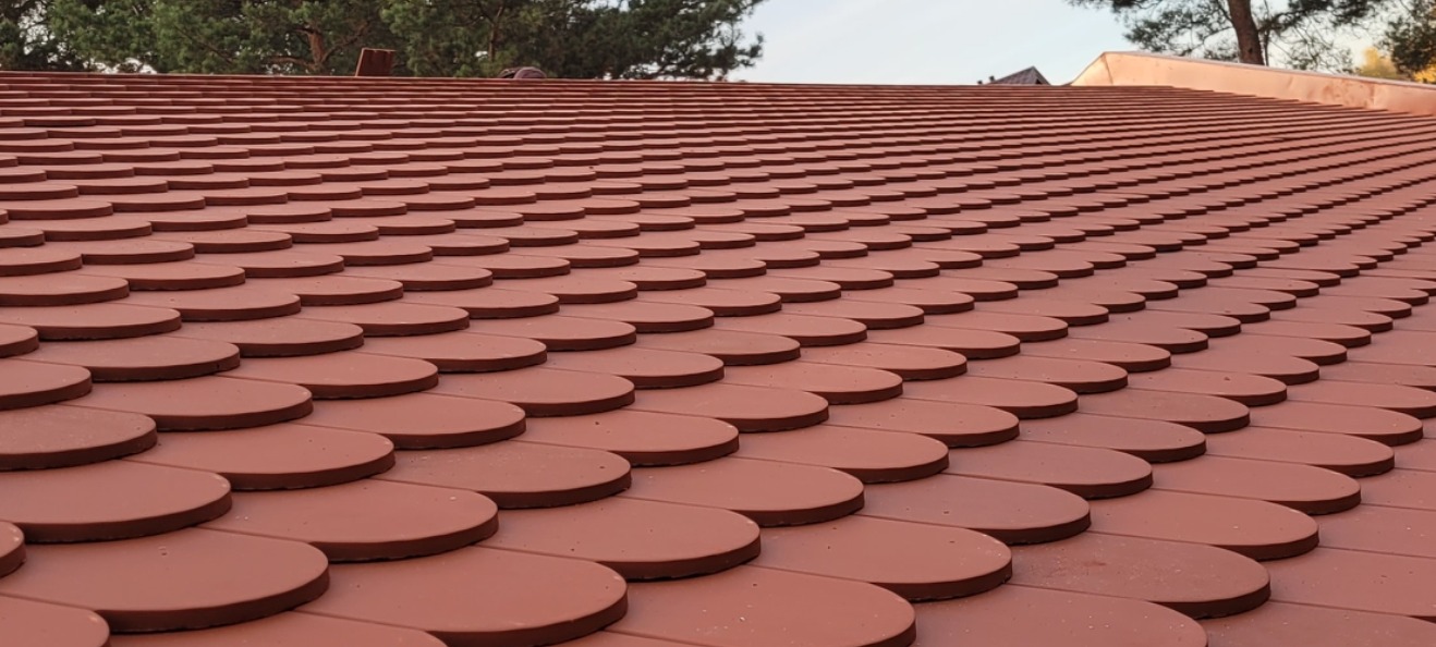 Nowy dach pokryty czerwoną dachówką ceramiczną w kształcie łuski, widok z dołu pod kątem z drzewami w tle.
