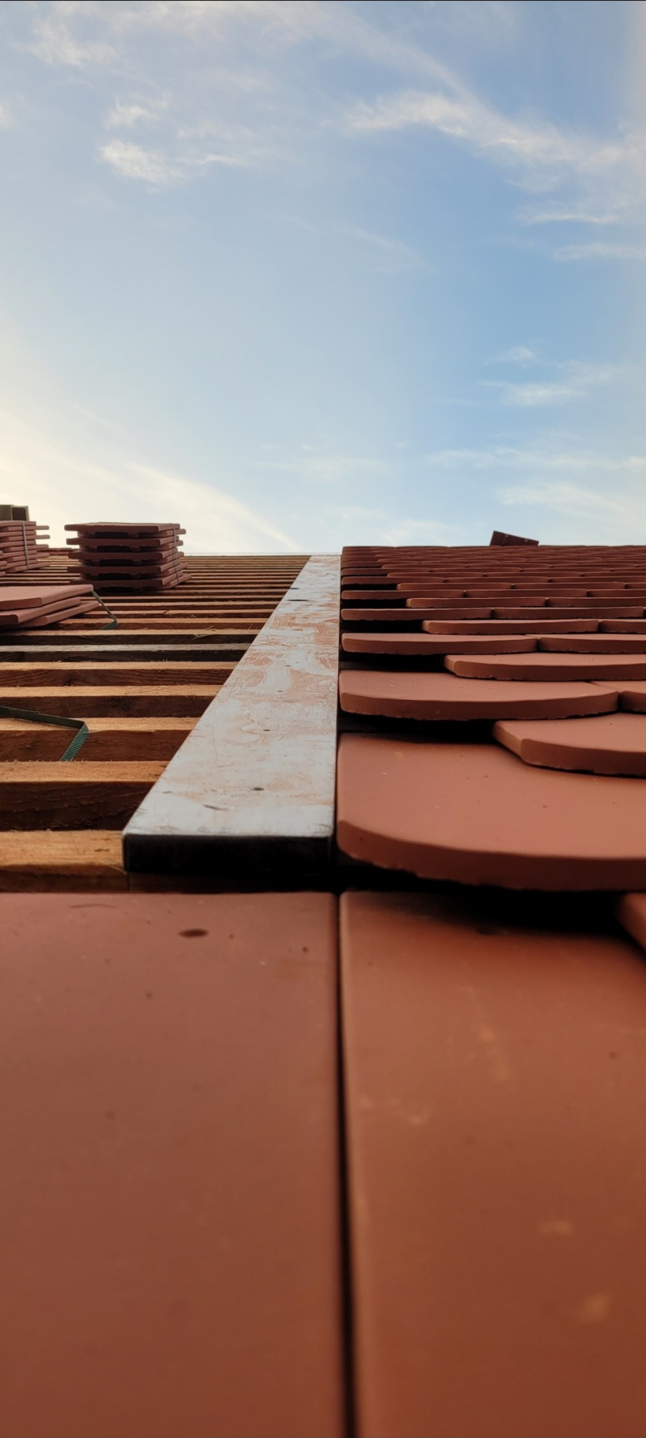 Montaż brązowej dachówki ceramicznej na drewnianej więźbie dachowej, widok z dołu na niebo.