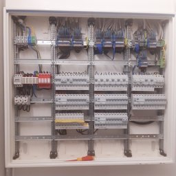Usługi elektryczne i ogólnobudowlane Rafał Turski - Otwarta skrzynka rozdzielcza z zamontowanymi bezpiecznikami, przewodami i szynami DIN, widoczny pomarańczowo-żółty śrubokręt na dnie obudowy.