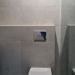 Usługi elektryczne i ogólnobudowlane Rafał Turski - Nowoczesna toaleta podwieszana z chromowanym przyciskiem spłukującym na tle szarych, teksturowanych płytek w wykończonej łazience z kabiną prysznicową.