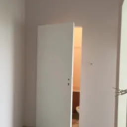 Pokój w trakcie malowania, z widocznymi narzędziami malarskimi, otwartymi drzwiami do łazienki i świeżo pomalowanymi ścianami w odcieniach beżu.