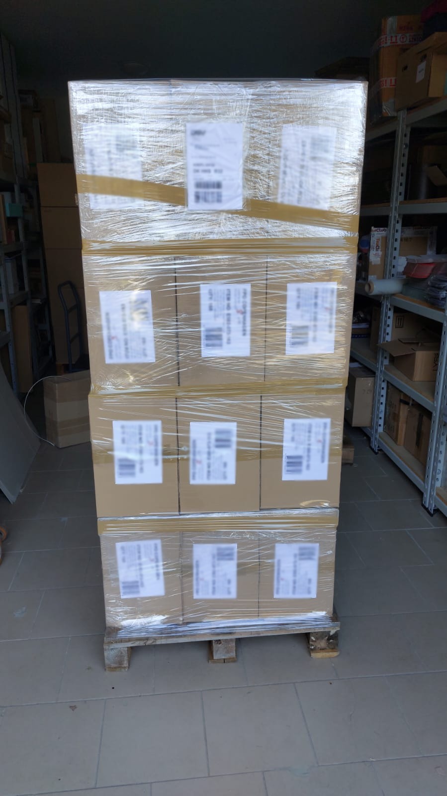 Paleta z kartonami owinięta folią stretch, zabezpieczona taśmą, z naklejonymi etykietami adresowymi, widok z bliska w magazynie.
