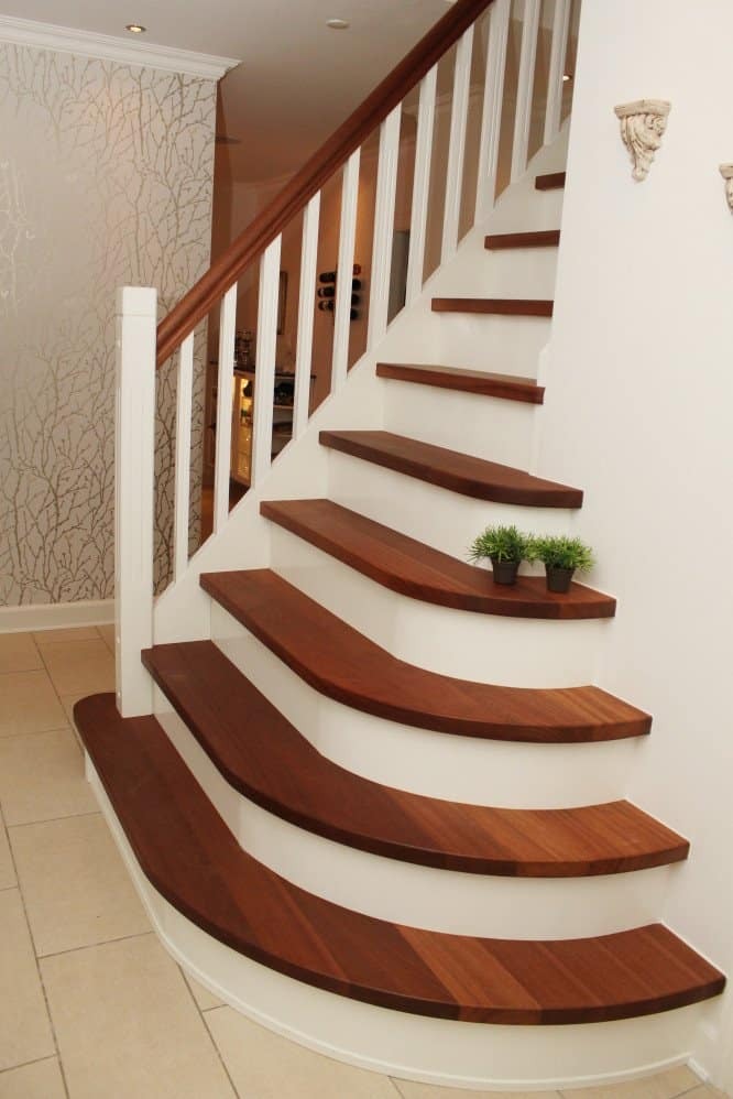 Zakrzywione schody z ciemnego drewna z białymi podstopnicami i balustradą, udekorowane małymi doniczkami z zielenią na jednym ze stopni.