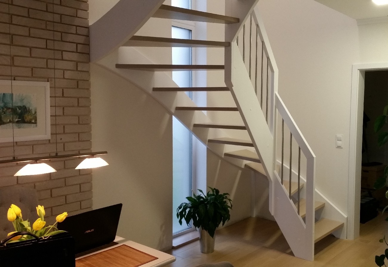 Nowoczesne schody z drewnianymi stopniami i białą balustradą w jasnym wnętrzu, widoczne z perspektywy biurka z laptopem i tulipanami.