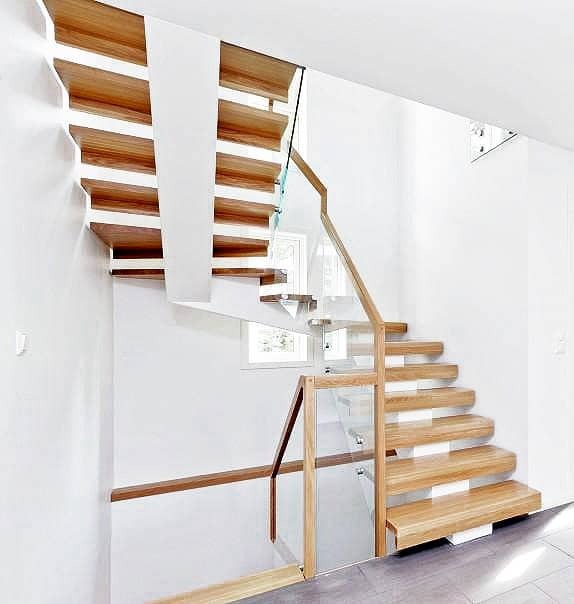 Nowoczesne schody z drewnianymi stopniami i szklaną balustradą w minimalistycznym, białym wnętrzu.