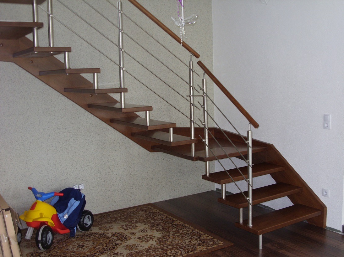 Nowoczesne schody z drewnianymi stopniami i metalową balustradą z cienkich prętów, widok z dołu, obok dziecięcy jeździk na dywanie.