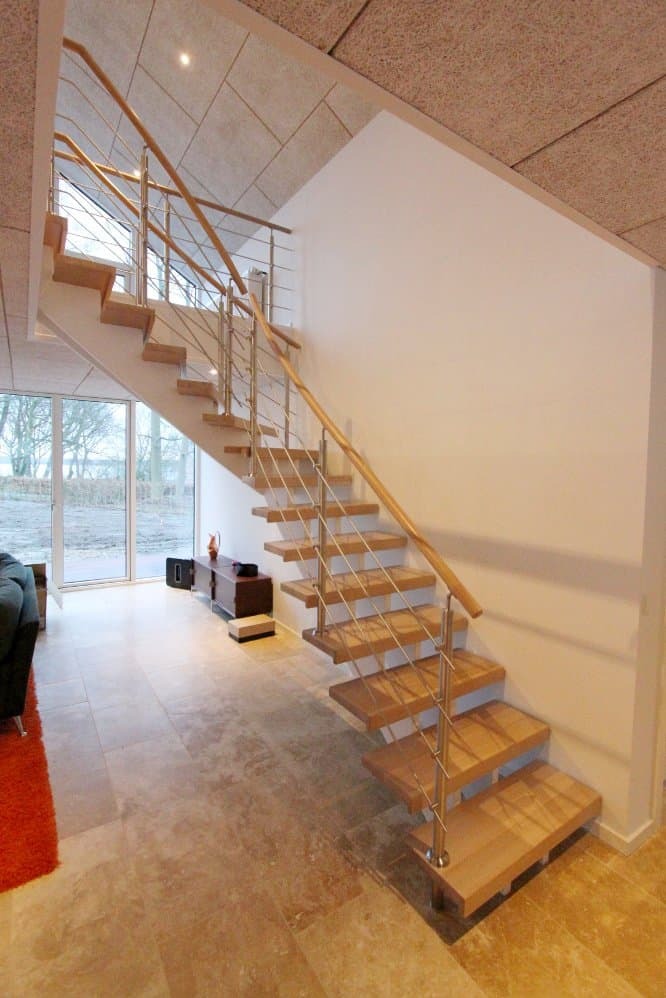 Nowoczesne schody z drewnianymi stopniami i metalową balustradą na tle jasnego wnętrza z dużym oknem.