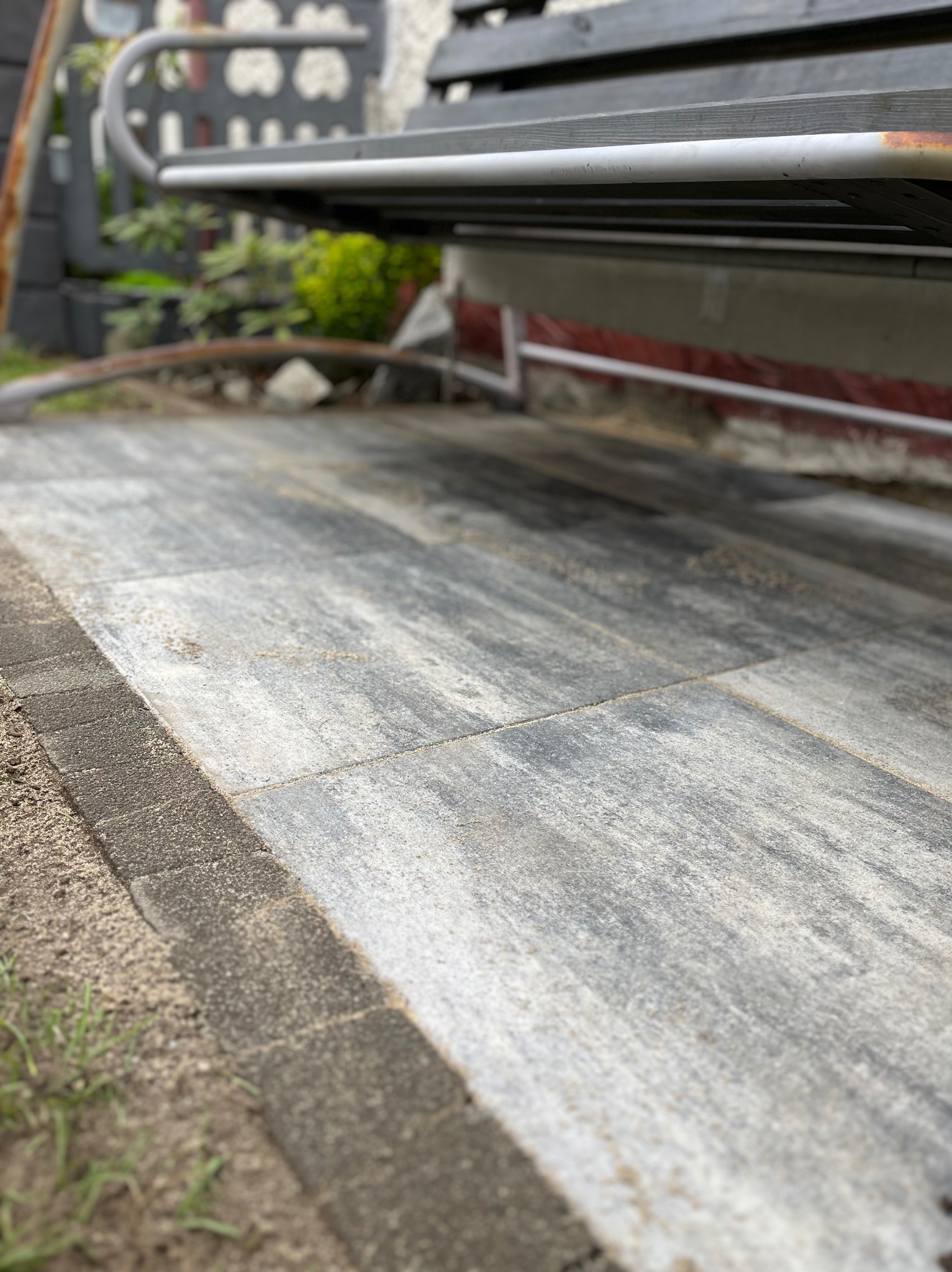 Świeżo ułożona, szara kostka brukowa na posesji, widok z perspektywy niskiego kąta, z fragmentem ławki w tle.