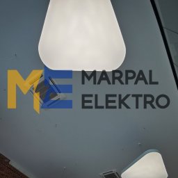 Marpal Elektro Sp. z o.o. - Widok z dołu na sufit z nowoczesnym oświetleniem w kształcie zaokrąglonych kwadratów, widoczny system klimatyzacji i logo firmy Marpal Elektro