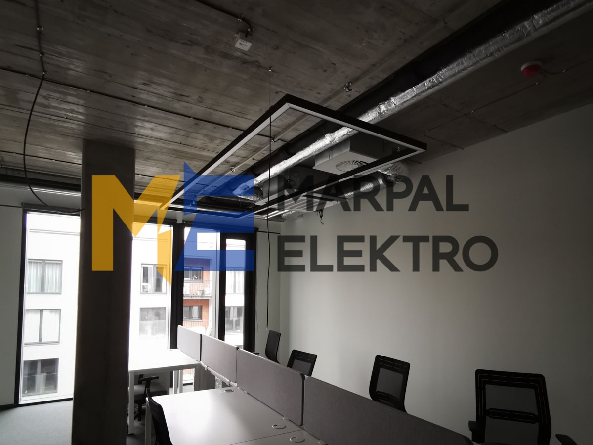 Nowoczesne biuro z zainstalowanym systemem oświetlenia liniowego pod sufitem, widoczne elementy instalacji elektrycznej i wentylacyjnej.