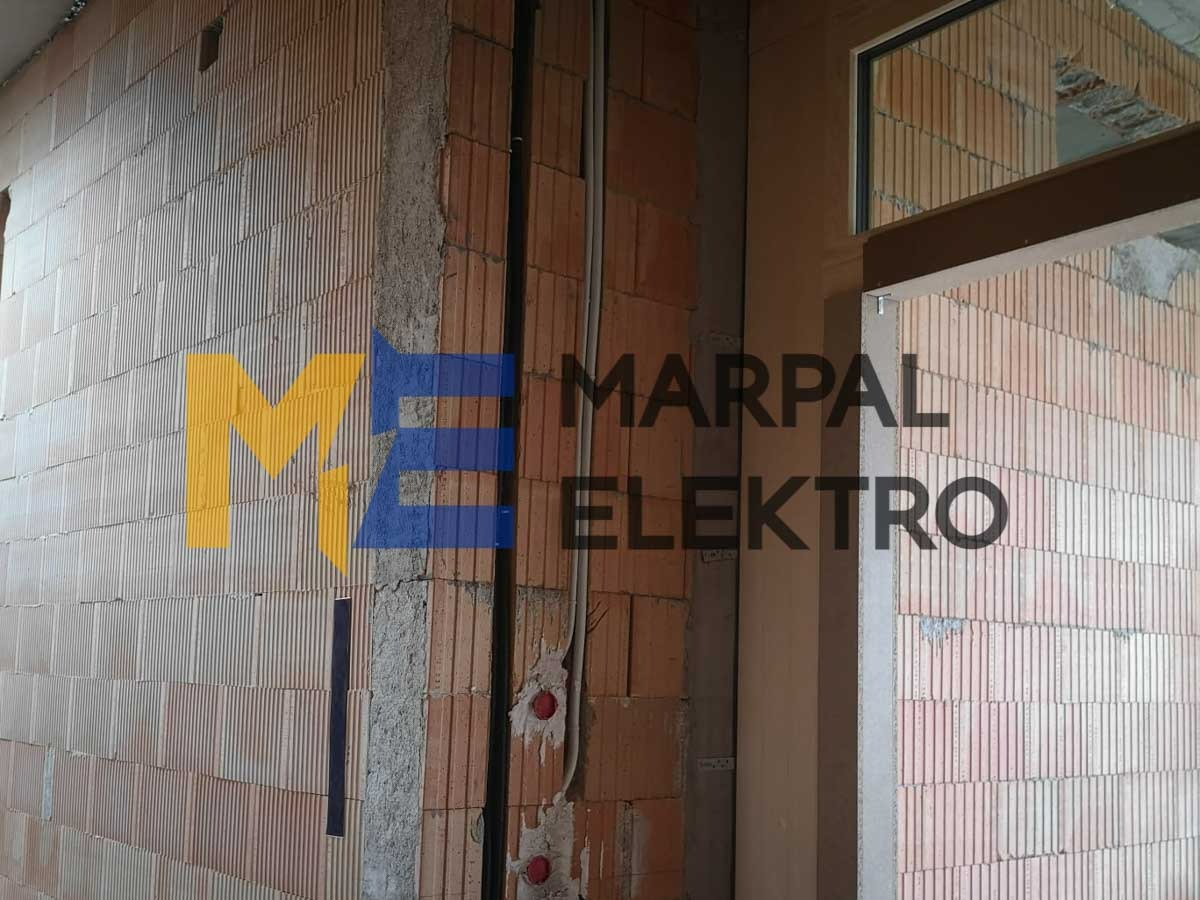 Ściana z czerwonej cegły z widocznymi przewodami elektrycznymi, instalacja podtynkowa, logo firmy Marpal Elektro na ścianie.