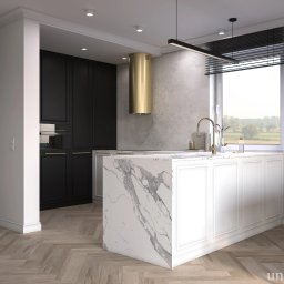 UNA STUDIO - Nowoczesna kuchnia z marmurową wyspą, złotym okapem i czarnymi szafkami, parkiet w jodełkę. Za oknem widok na zielone pola.