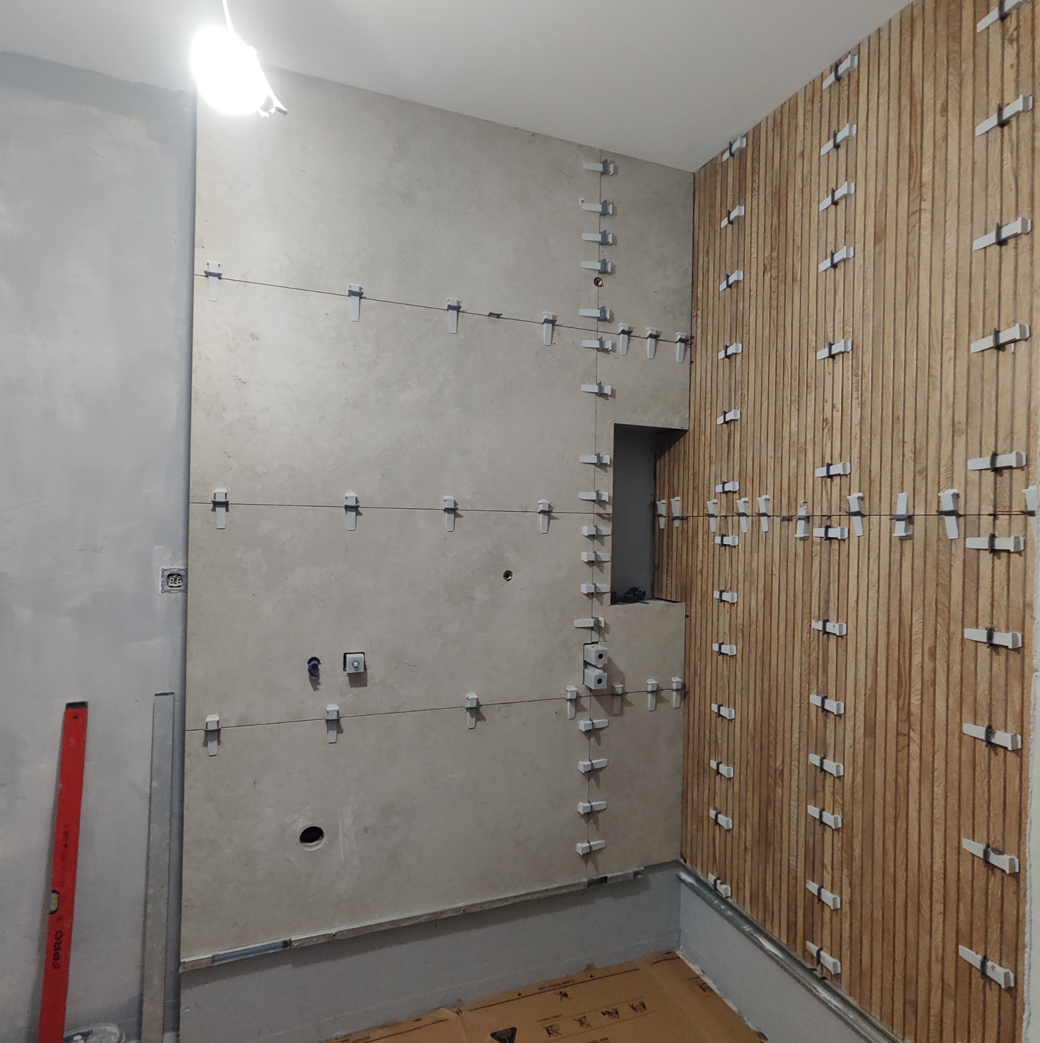Ściana w trakcie wykańczania płytkami imitującymi drewno, z widocznymi krzyżykami dystansowymi i poziomnicą, fragment ściany z gładzią.