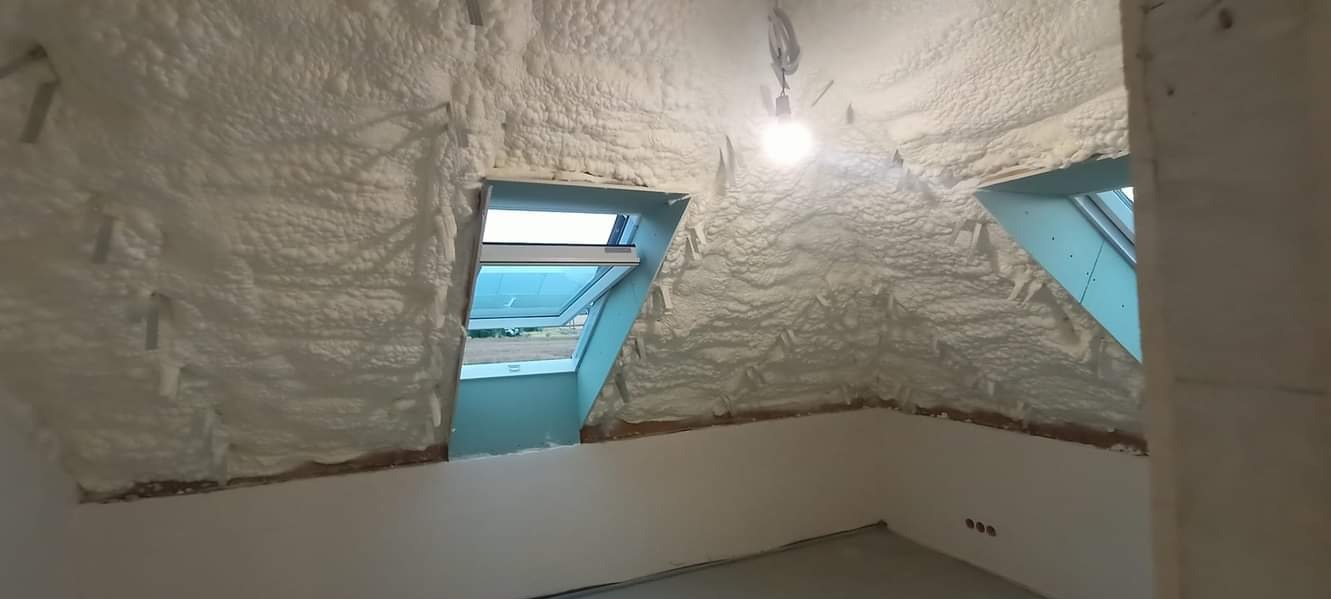 Poddasze po izolacji pianą PUR, widoczne dwa okna dachowe, ściany częściowo przygotowane do wykończenia, surowy stan.